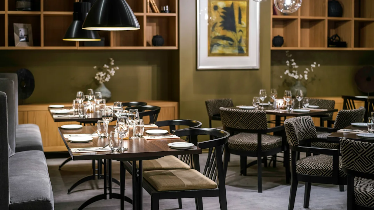 En hyggelig moderne restaurant med flot opdækkede borde, blød belysning og elegant indretning. Varme træfarver og stilfulde møbler skaber en indbydende stemning til en dejlig middag.