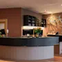 A stylish hotel reception and bar area with a curved counter, monitors, flowers, and a bicycle mounted on a brown wall.