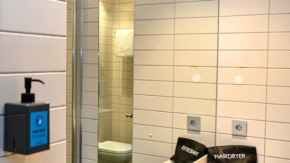 A bright bathroom with a sink, mirror, and a reflection of a toilet. Hand wash and hairdryer are provided. Text says Fresh and Drinkable Tap Water.