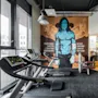 Treadmills sit stationary in a gym, facing a mural of a blue-skinned figure. Text reads: "MY ROCK&ROLL IS BETTER THAN YOUR BODYBUILDING BUT NOT EVERYBODY CAN PLAY THAT GOOD."