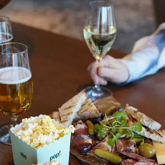 En person njuter av en charkbricka med vin, öl och popcorn märkta 'me pop!', vilket skapar en avslappnad och social atmosfär.