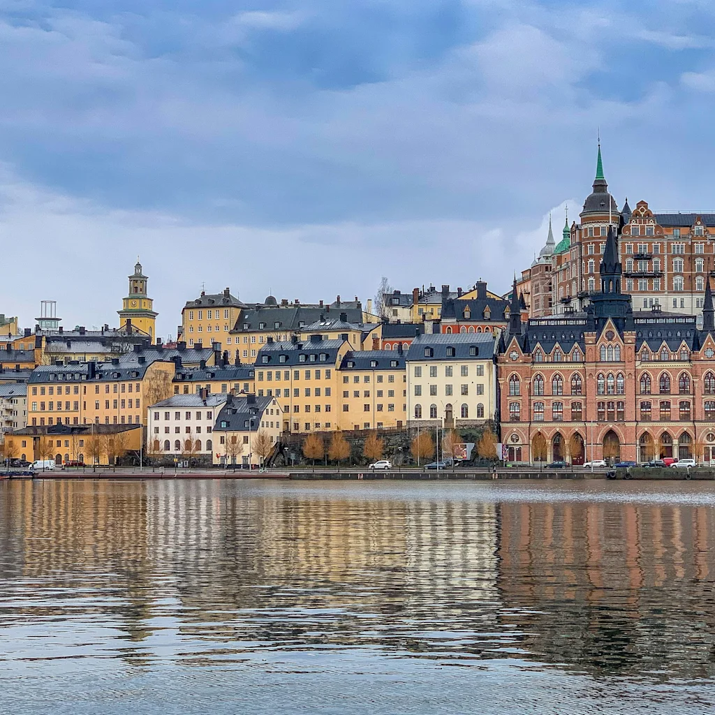 Stockholms bybilde med historiske bygninger speilet i vannet under en skyet himmel.