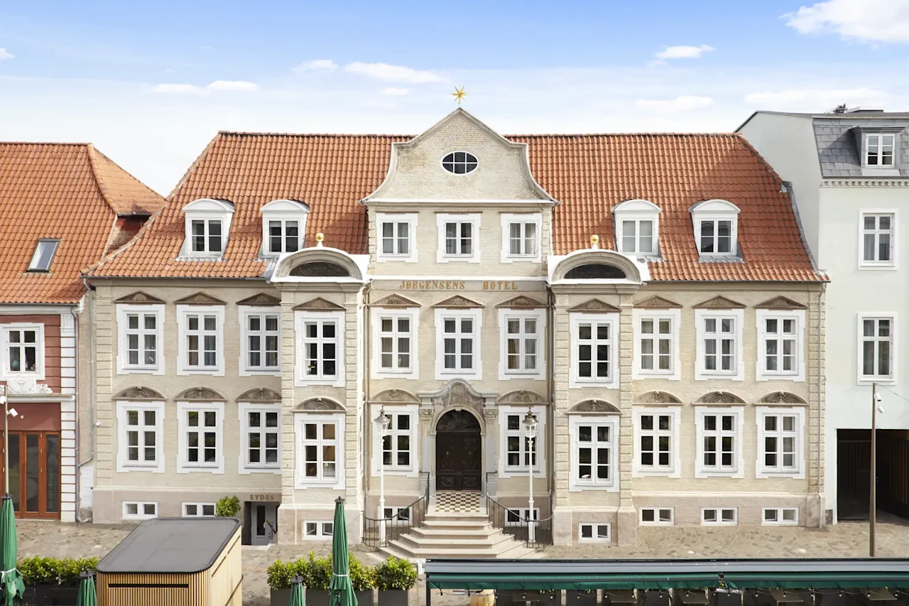 En storslået, historisk hotelbygning med rødt tegltag, mange vinduer og en fremtrædende indgang. Teksten HOTEL er synlig.