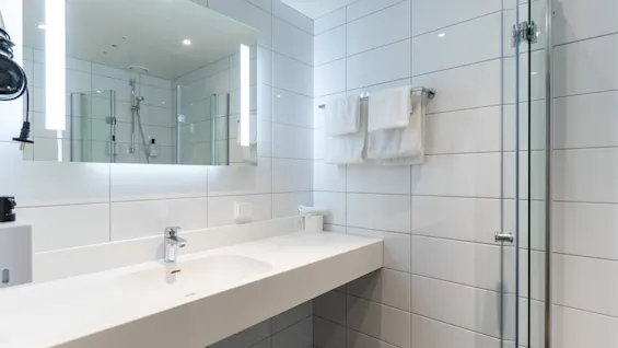 Et moderne og funksjonelt bad med en romslig servant, et opplyst speil og en dusjkabinett i glass.