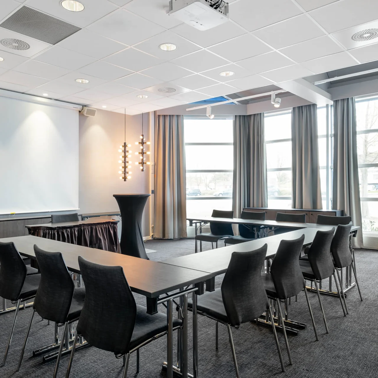 Conference room with a U-shaped table layout, empty chairs, a projector, and natural lighting from large windows.