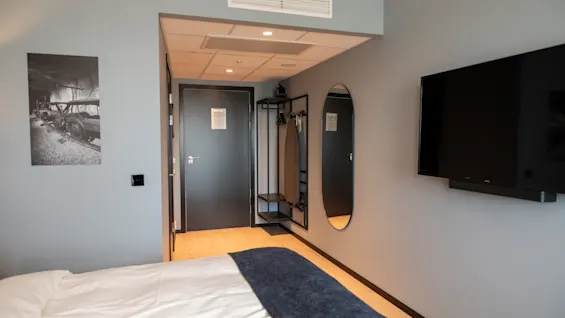 Et moderne hotellrom med en koselig seng, en veggmontert TV og et slående svart-hvitt kunstverk.