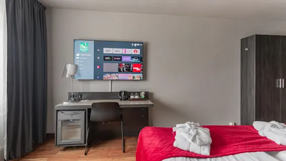 A modern hotel room featuring a large TV with channel options like svt1, svt2, svt play, a comfortable bed, and a desk.