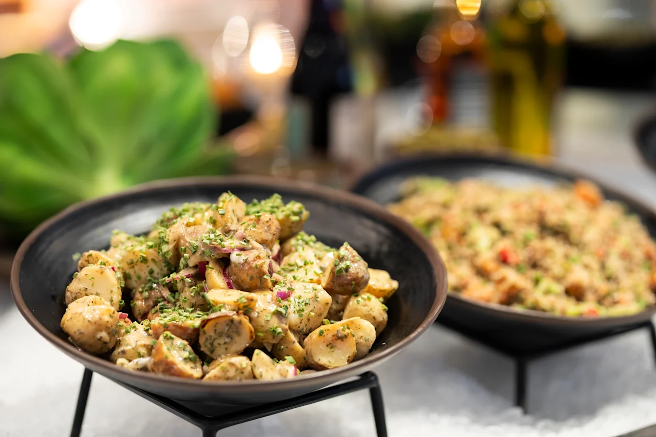 Lähikuva herkullisesta perunasalaatista yrteillä ja punasipulilla, osana suurempaa noutopöytää.