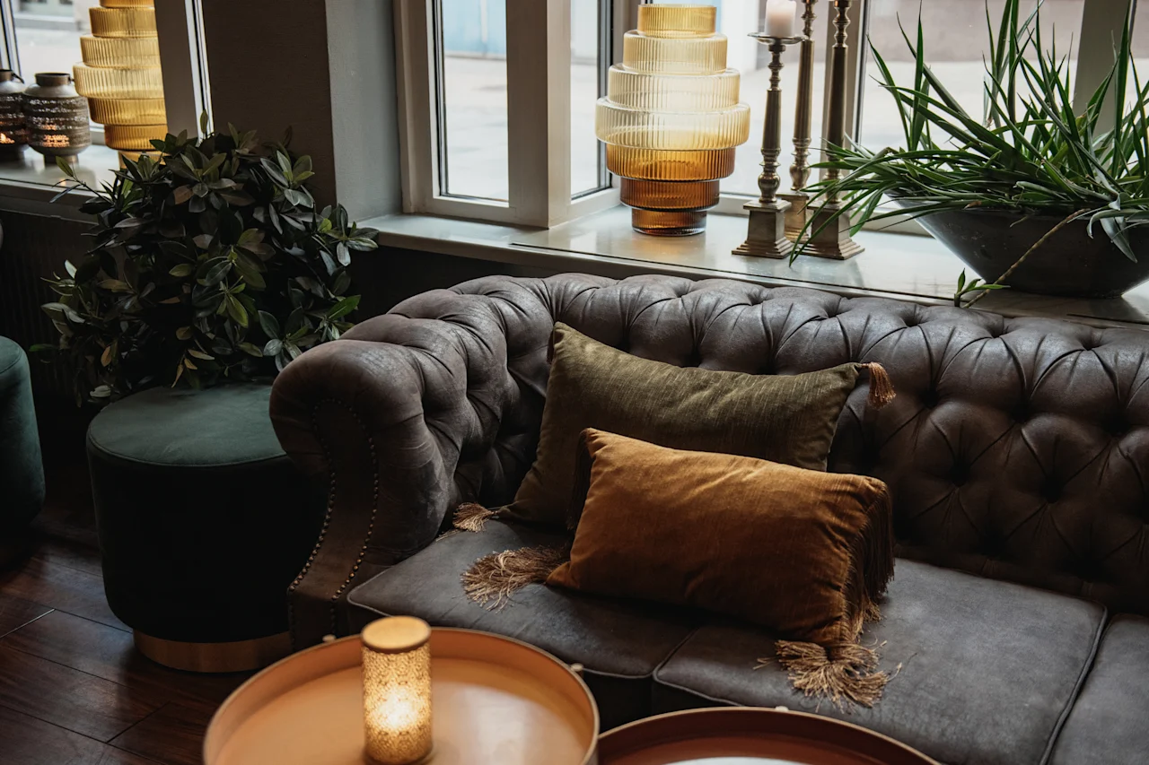 En bekväm och inbjudande loungeavdelning med en tuftad soffa med plyschkuddar, stämningsbelysning och frodig grönska.