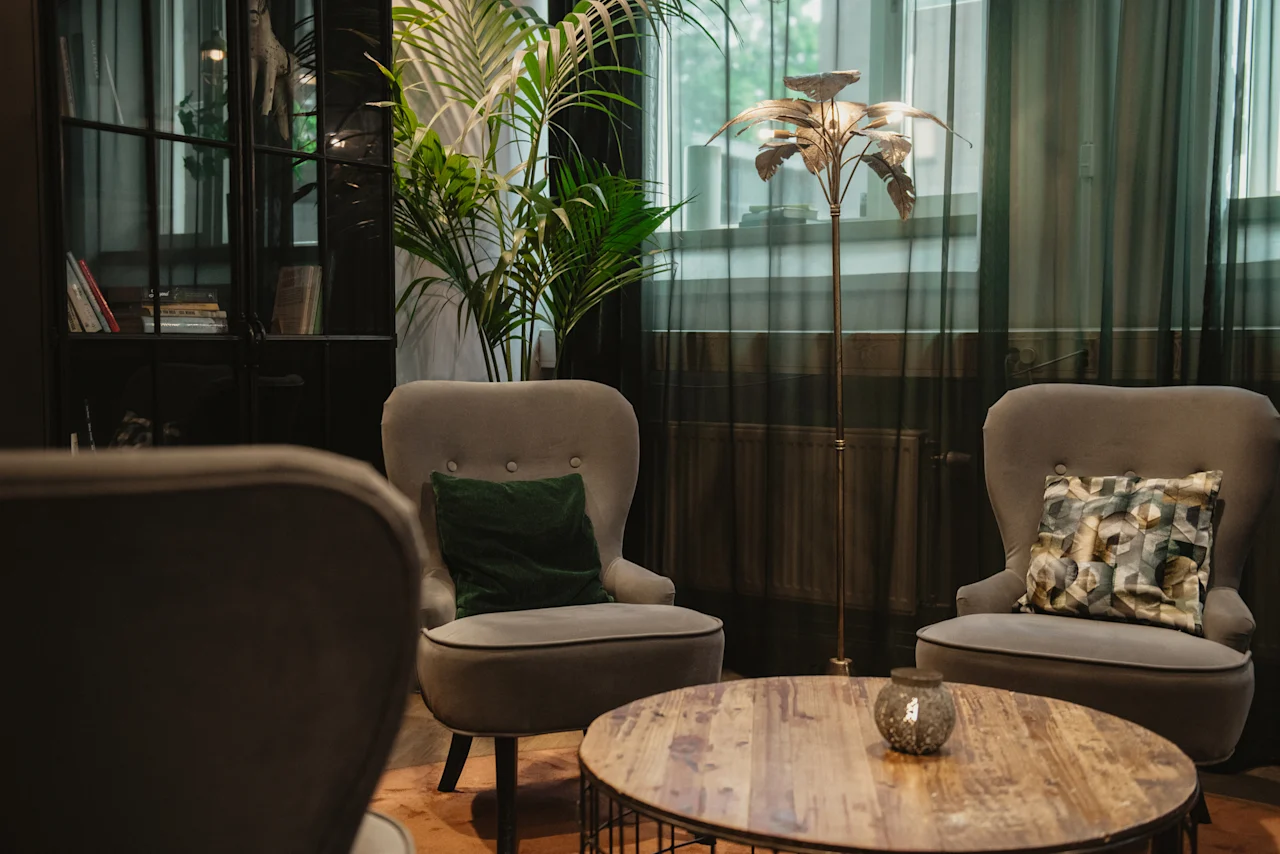 A cozy lounge area at Home Hotel Uppsala with two armchairs, a wooden coffee table, a plant, and a decorative floor lamp.