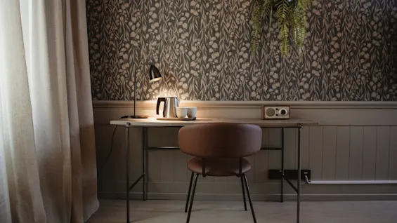 A functional and inviting desk space featuring a lamp, kettle, and radio, against a backdrop of botanical wallpaper.