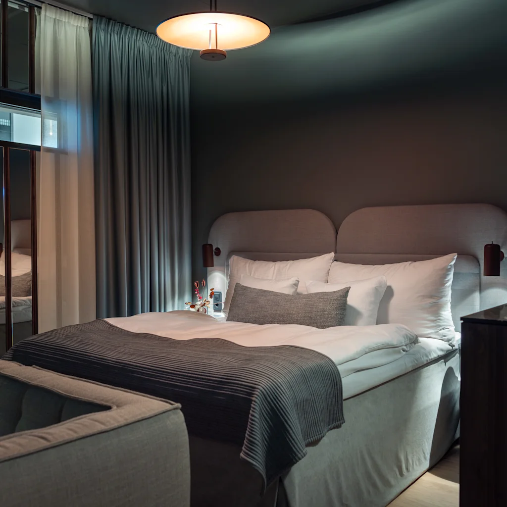 Et koselig hotellrom med en komfortabel seng og en sofa, med dempet belysning og myke møbler for et avslappende opphold.