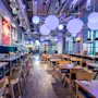 A modern restaurant features wooden tables, chairs, colorful wall art, and large spherical lights hanging from the ceiling, creating a lively and inviting atmosphere.