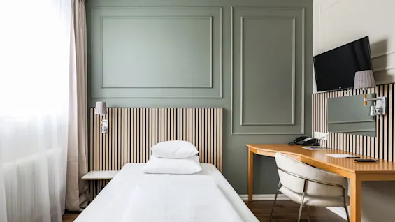 Viihtyisä hotellihuone Comfort Hotel Linköping Cityssä, jossa on sänky, työpöytä ja TV, vihreät seinät ja puuyksityiskohdat.