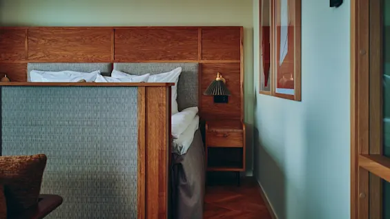 Et varmt og innbydende hotellrom med en sengegavl i tre, en stilig mønstret romdeler og en nattbordslampe.