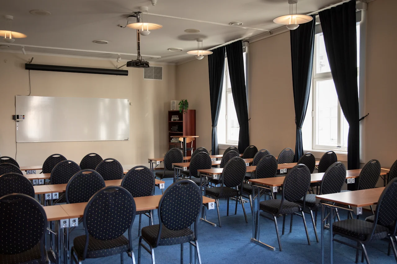 Et lokale indrettet til en præsentation eller forelæsning, med projektor, whiteboard og flere siddepladser.