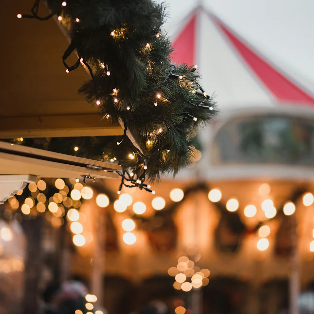 Festlig scene med glitrende lys og grøn guirlande, et rødt og hvidt telt i den slørede baggrund.
