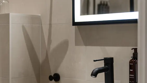 Et moderne badeværelse med håndvask, sort armatur og et oplyst spejl. En sæbedispenser mærket SOAP er synlig.
