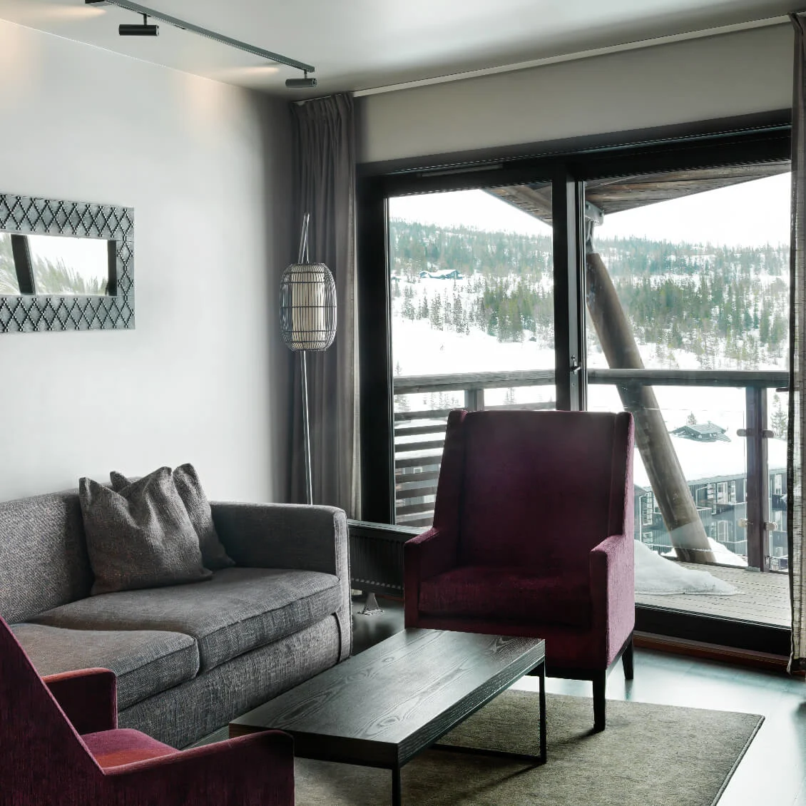 A modern living room features a grey sofa, two purple armchairs, and a black coffee table; a large window reveals a snowy landscape and wooden balcony outside.