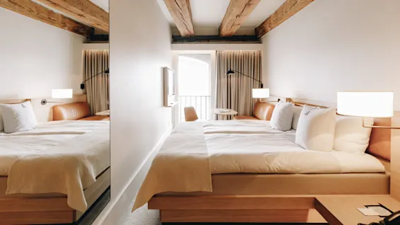 Ett ljust och modernt hotellrum med två bekväma sängar, takbjälkar i trä och en balkong för avkoppling.