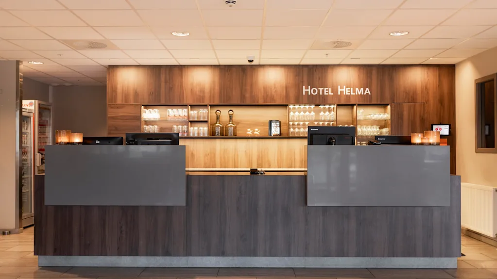 Et moderne hotelreceptionsområde med en trædisk og oplyste hylder. Teksten HOTEL HELMA vises ovenfor, klar til gæster.