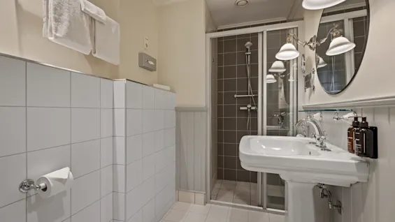 Et rent og moderne badeværelse med en hvid håndvask, en glasindkapslet bruser og friske håndklæder.