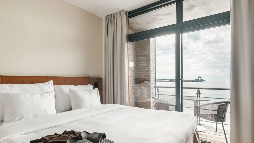 A comfortable hotel room at Farris Bad in Larvik with a bed, slippers, and a robe, featuring a balcony overlooking the sea.