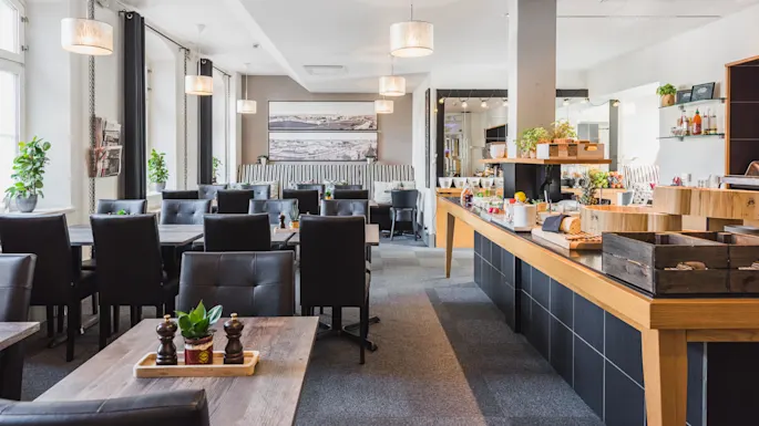 Et tomt restaurantinteriør med bord, stoler og en bufféinnredning, klar til servering.