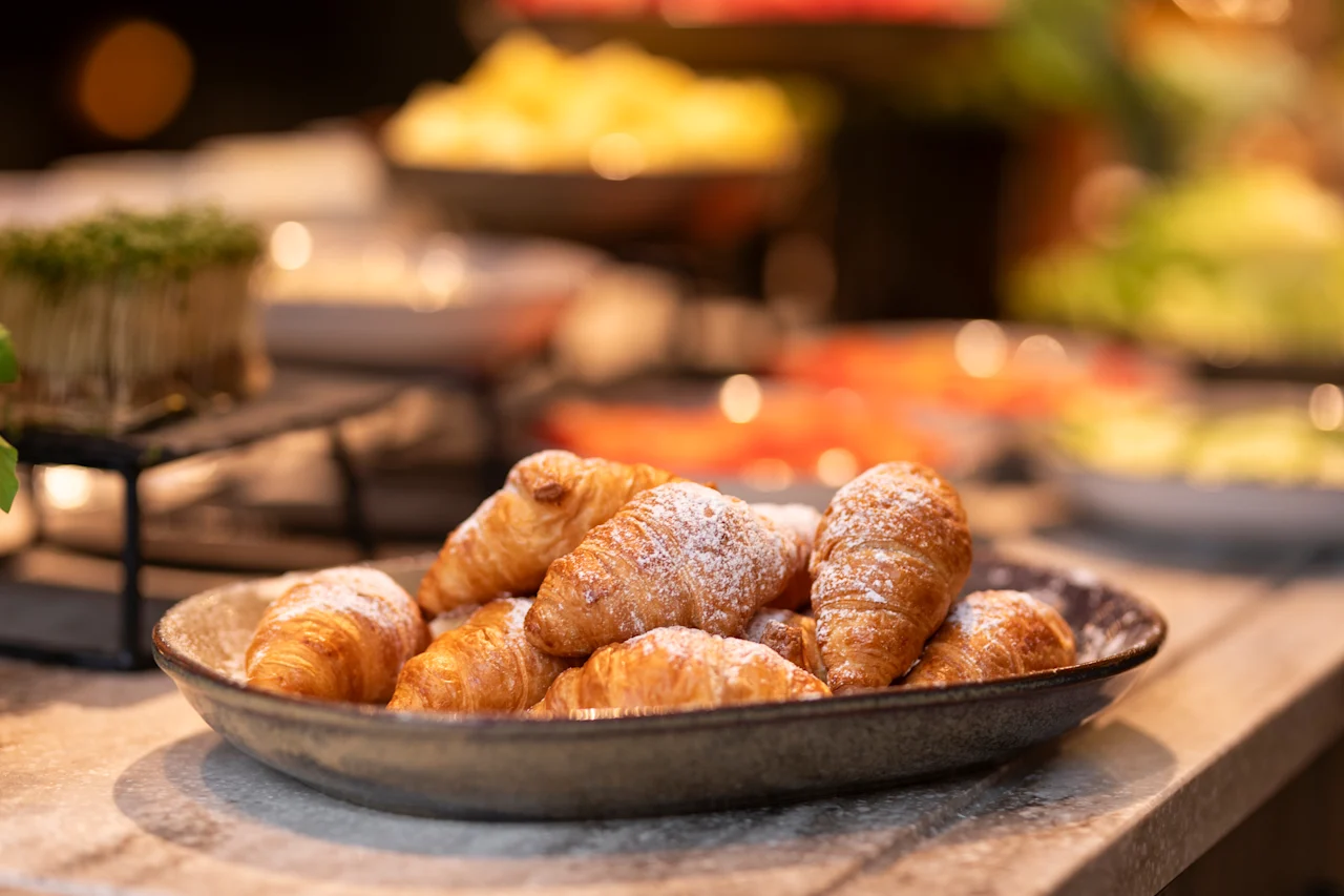 Lautanen kultaisia croissanteja tomusokerilla, valmiina nautittavaksi buffetissa.