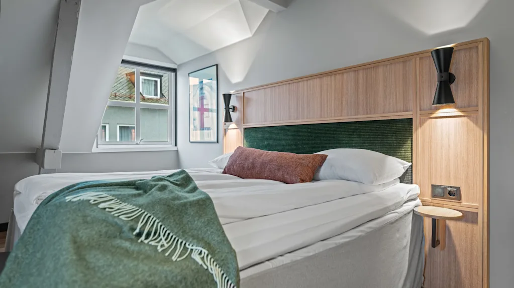 Et hyggeligt hotelværelse med en komfortabel seng, et grønt tæppe og et vindue, der giver et glimt af omverdenen.