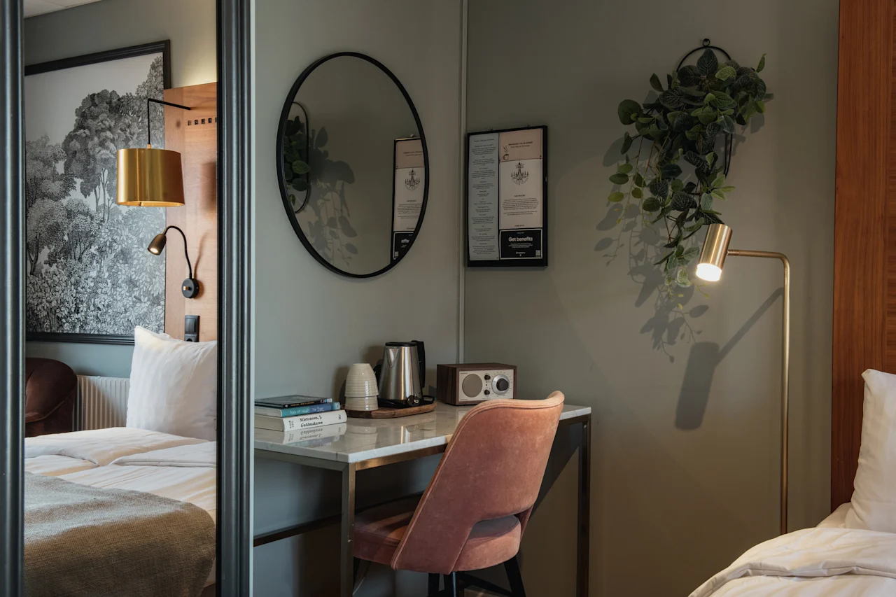 Et koselig hotellrom med en komfortabel seng og et velutstyrt skrivebordsområde, med vannkoker, bøker og en radio. Getbonello