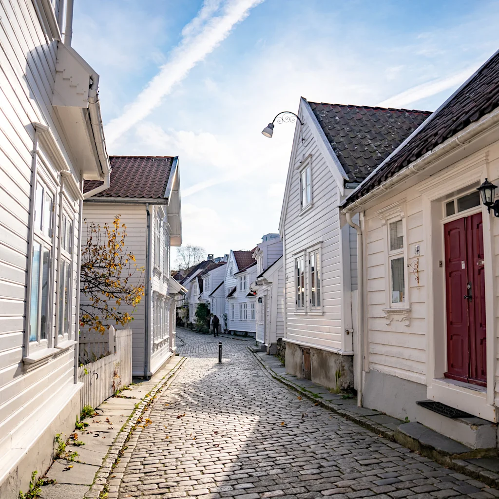 Viehättävä mukulakivikatu, jota reunustavat perinteiset valkoiset puutalot kirkkaan sinisen taivaan alla, ja yhdessä talossa on punainen ovi.