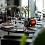 Et vakkert dekket restaurantbord med glass, bestikk, servietter, blomster og et glødende lys, klart for middag.