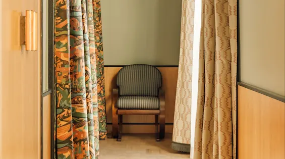 En elegant korridor med mønstrede gardiner og en stripet stoppet stol, som antyder et rolig interiør.