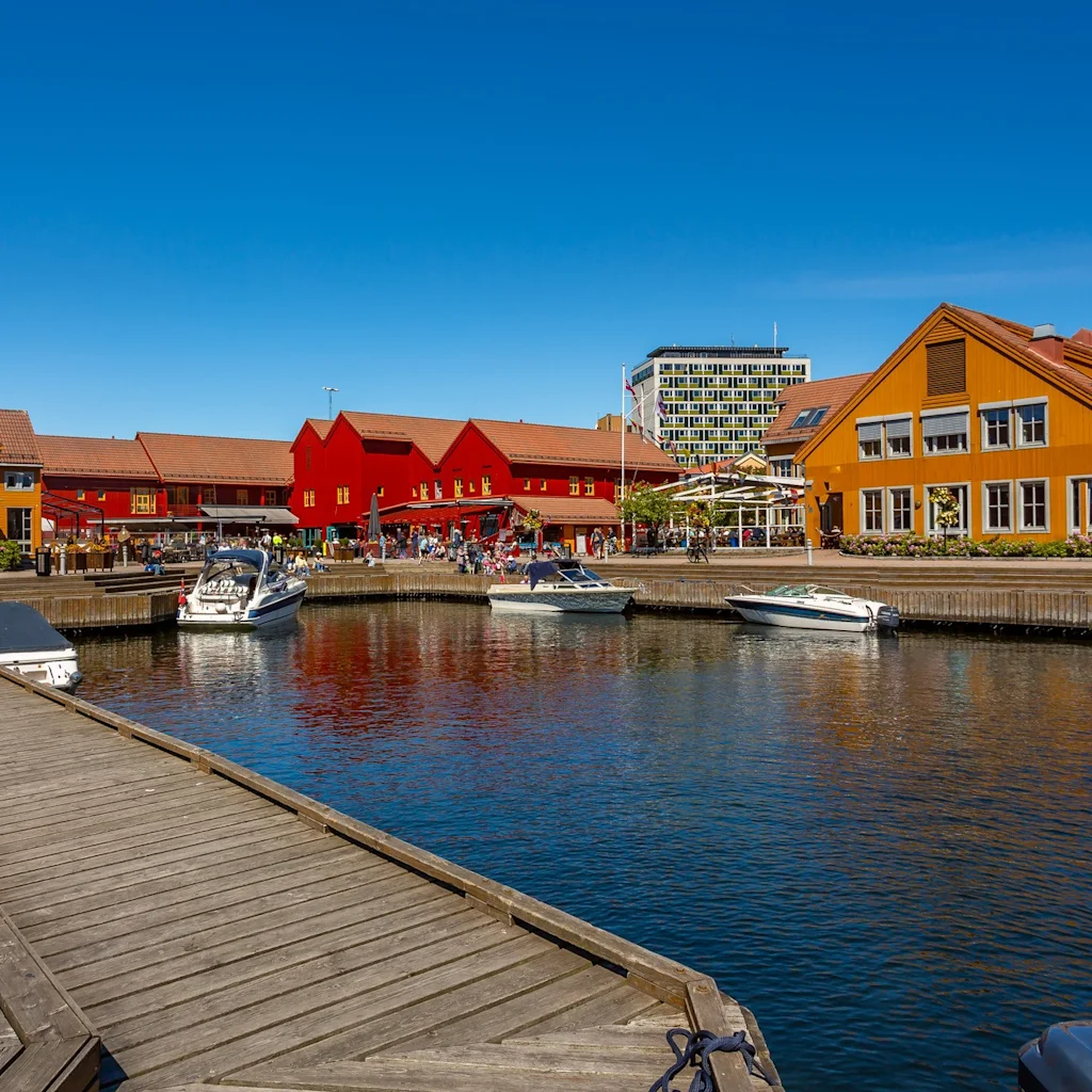 En livlig hamnscen med färgglada byggnader, båtar förtöjda längs en brygga och en klarblå himmel.