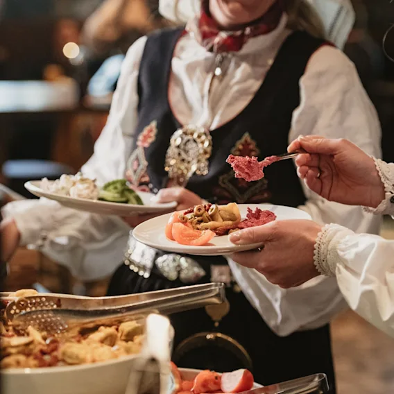 Gjester i bunad som forsyner seg med mat fra et festdekket buffetbord.