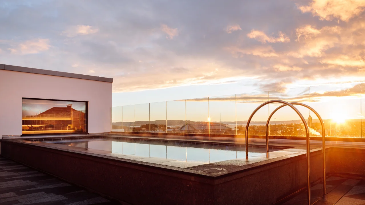 Rooftop pool at sunset with a clear view of the horizon and colorful clouds.