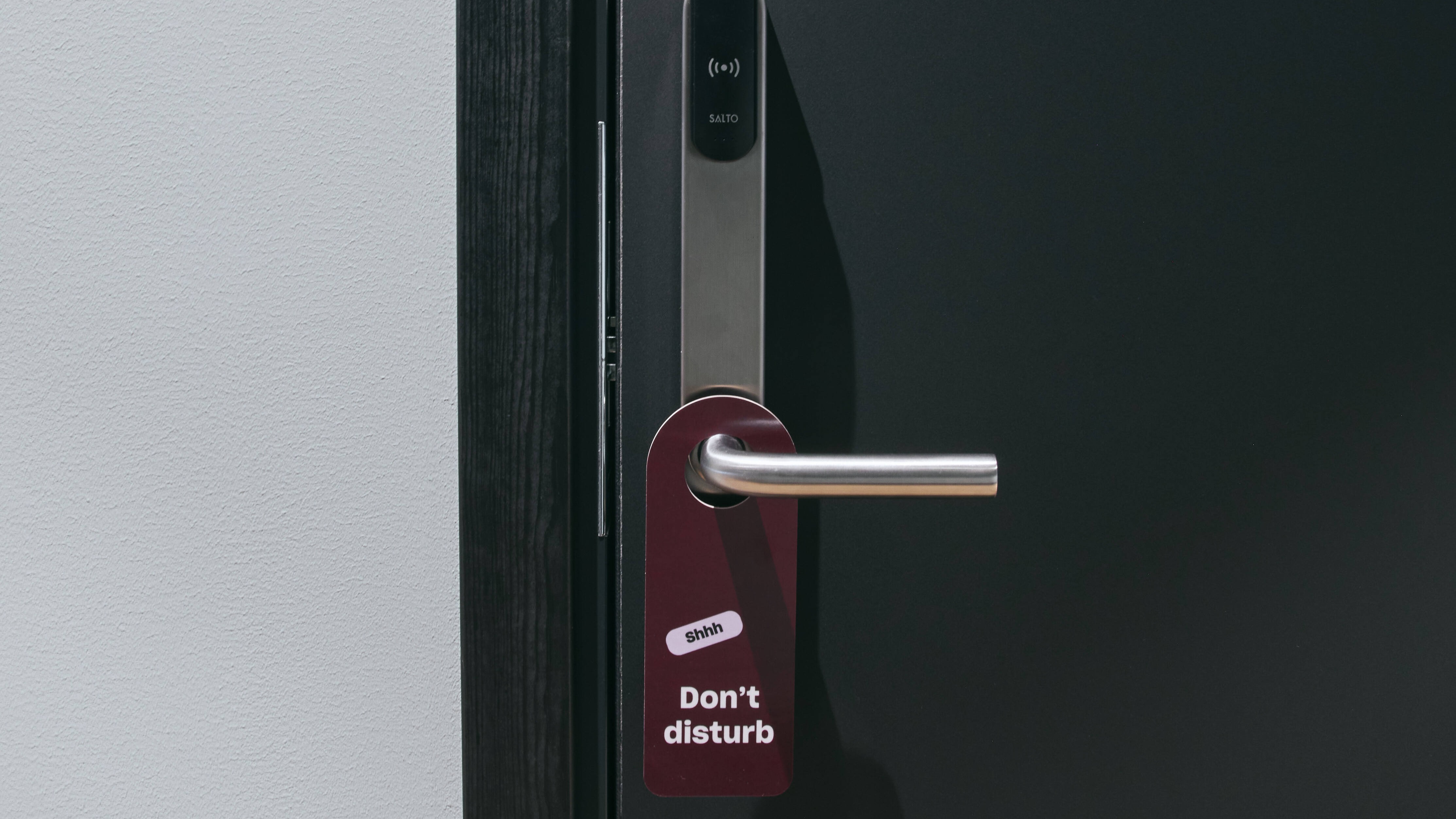 En hotellrumsdörr med en 'Shhh Stör ej' skylt hängande från handtaget, vilket indikerar avskildhet.