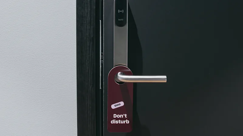 En hotelværelsesdør med et 'Shhh Forstyr ikke' skilt hængende fra håndtaget, der indikerer privatliv.