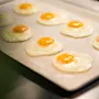 A close-up of several sunny-side up eggs cooking on a flat surface, ready to be served for breakfast.