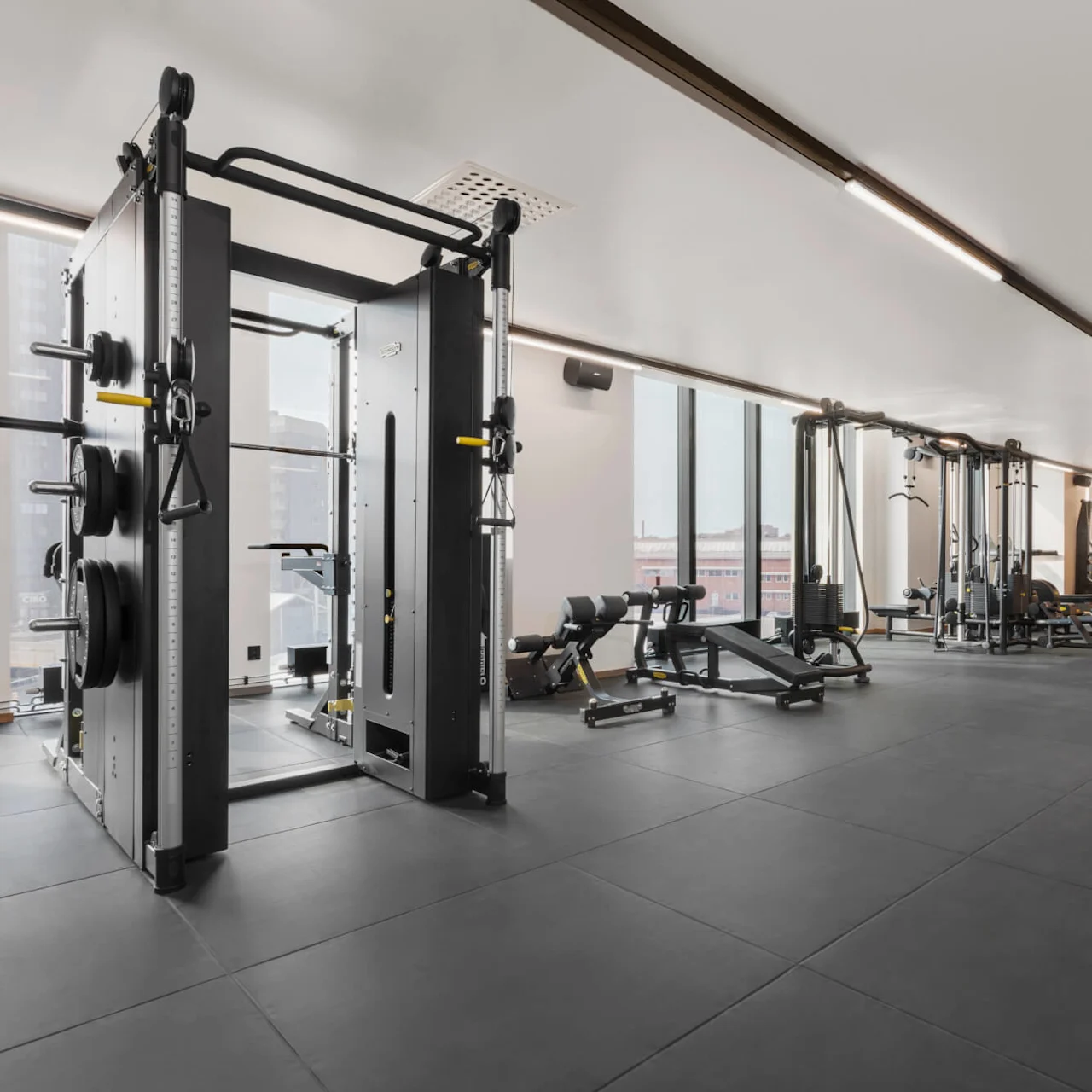 Ett gym med viktmaskiner och bänkar organiserade i ett rymligt, väl upplyst rum. Stora fönster erbjuder utsikt utanför och förstärker den öppna, moderna miljön.