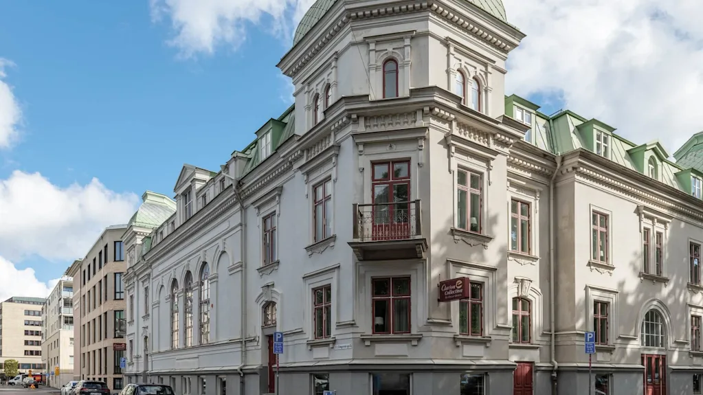 A neo-classical building with a green dome, parked cars on a quiet street, blue sky with clouds.