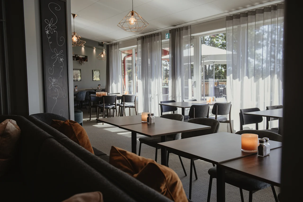 En ljus och inbjudande restaurangmatsal med bord, stolar och stora fönster som vetter mot en uteservering.