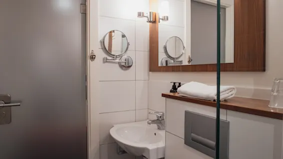 Home Hotel Kung Oscar offers a bright and modern bathroom with a clean sink, mirror, and fresh towel for a comfortable stay.
