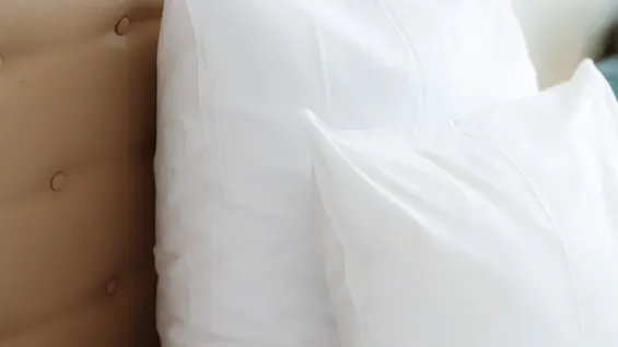 Et nærbillede af en redt seng med bløde hvide puder og en lys, tuftet sengegavl, der indbyder til komfort og afslapning.