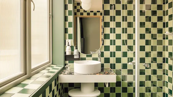 Hobo Oslo: A vibrant bathroom with green and light green checkered tiles, a sleek sink, and a glass shower.