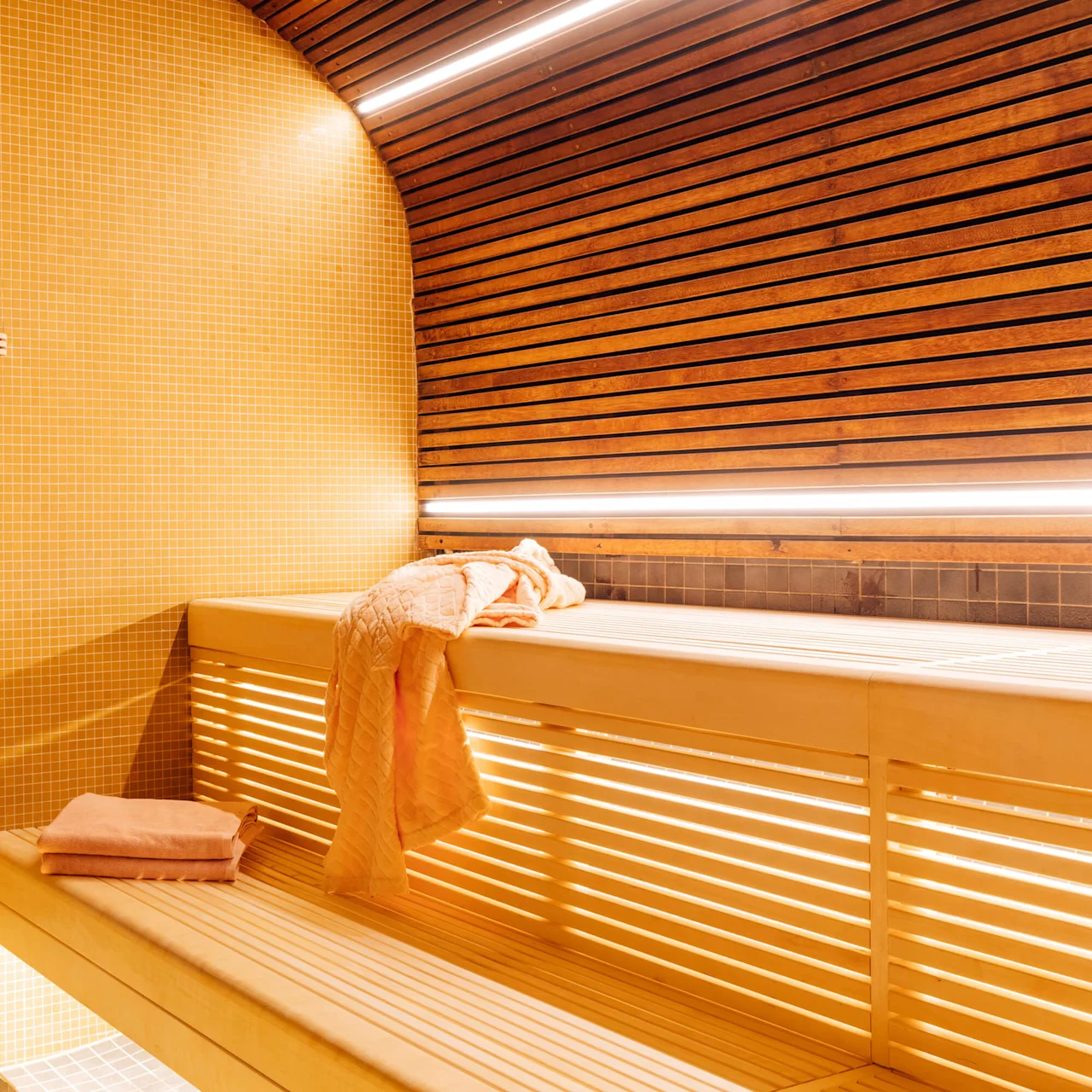 En sauna med træbænke og gule fliser, et håndklæde draperet over en bænk.