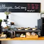 En frokostbuffet har korn, en brødrister, brød og bakverk på en trebenk. På en tavle over står det: "Allergies...Don't Worry. We got you! Dairy free, Gluten free, Nut free."