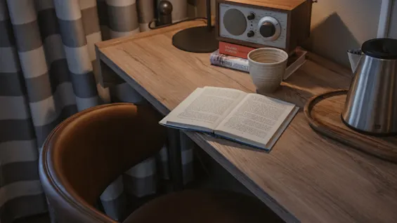 A cozy desk setup with an open book, a warm drink, and a radio, inviting relaxation.