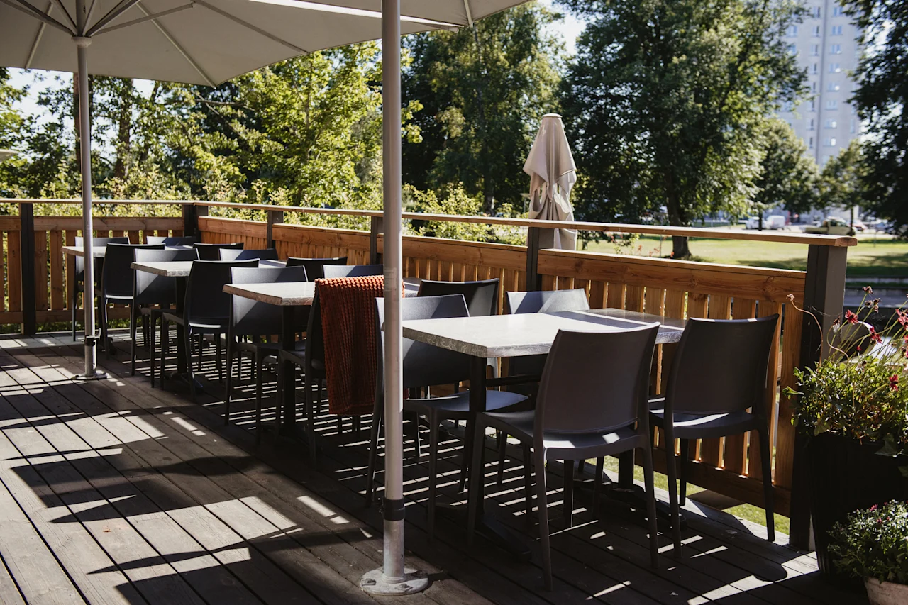 En inbjudande uteplats med bord och stolar under stora parasoller, omgiven av lummiga gröna träd, perfekt för middag.